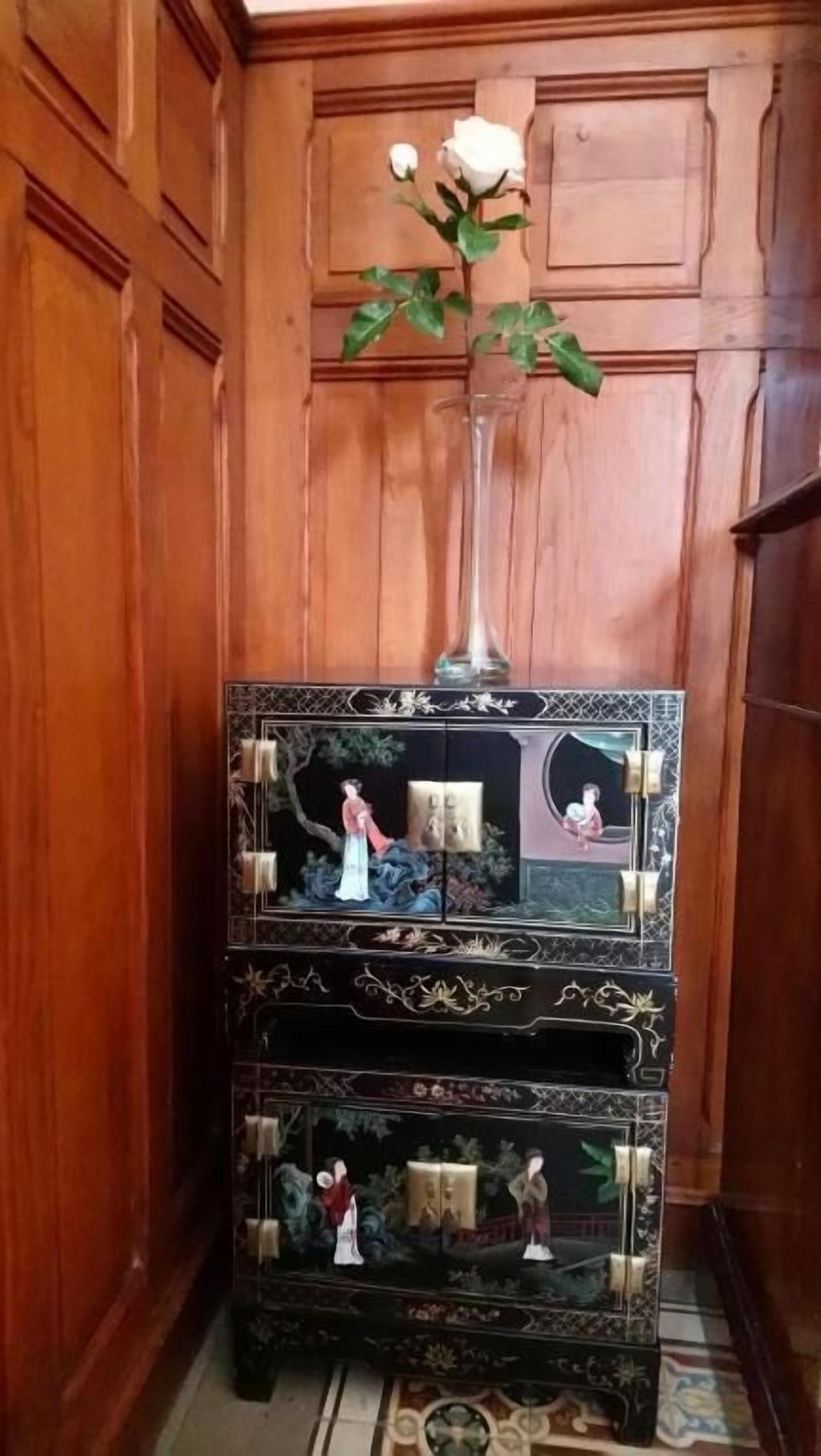 Een houten kastier met ingewikkelde gravures en een vaas met een witte roos.