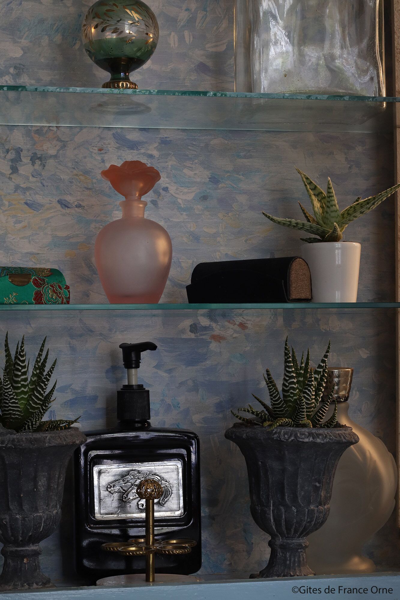 A shelf with a globe, a pink vase, a potted plant, a black perfume bottle, and two potted plants.