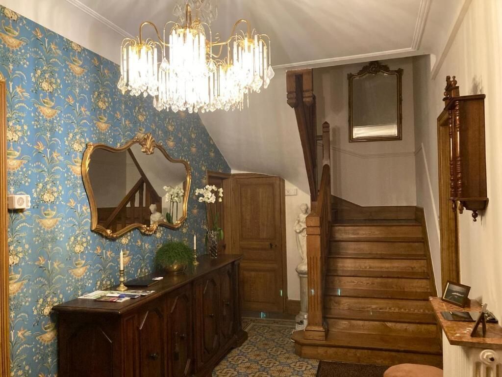 A staircase with a wooden finish, a chandelier, a mirror, and a patterned wallpaper.