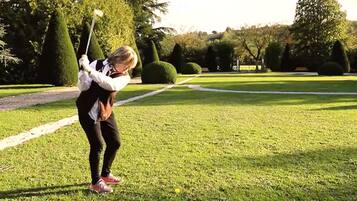 Una persona jugando golf sobre un césped impecable, con árboles y arbustos cuidadosamente podados al fondo.