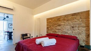 Ein Hotelzimmer mit einer Wand aus Steinoptik, einer roten Bettdecke und zwei aufgerollten Handtüchern auf dem Bett.