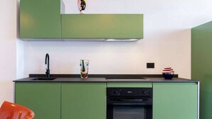 Eine kleine Küche mit grünen Schränken, einer schwarzen Arbeitsplatte, einem Spülbecken, einem Geschirrspüler und einem Backofen.