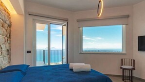 Ein Schlafzimmer mit einem großen Bett, Meerblick und einer Steinsäule.