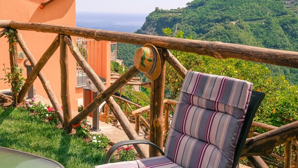 Un balcon avec une balustrade en bois, un coussin à rayures et une vue sur une colline verdoyante.
