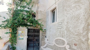 Une ruelle étroite, avec un portail en métal noir, une petite fenêtre et une pancarte indiquant la présence d’un jardin.