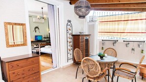 A room with a wooden dresser, wicker chairs, a round table, and a hanging light fixture. - Amazing apartment with view (Piraeus)