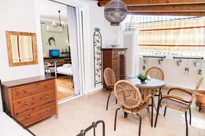 Relax in this open-plan living space with a dining area, featuring a wooden cabinet, wicker chairs, and a hanging light fixture.