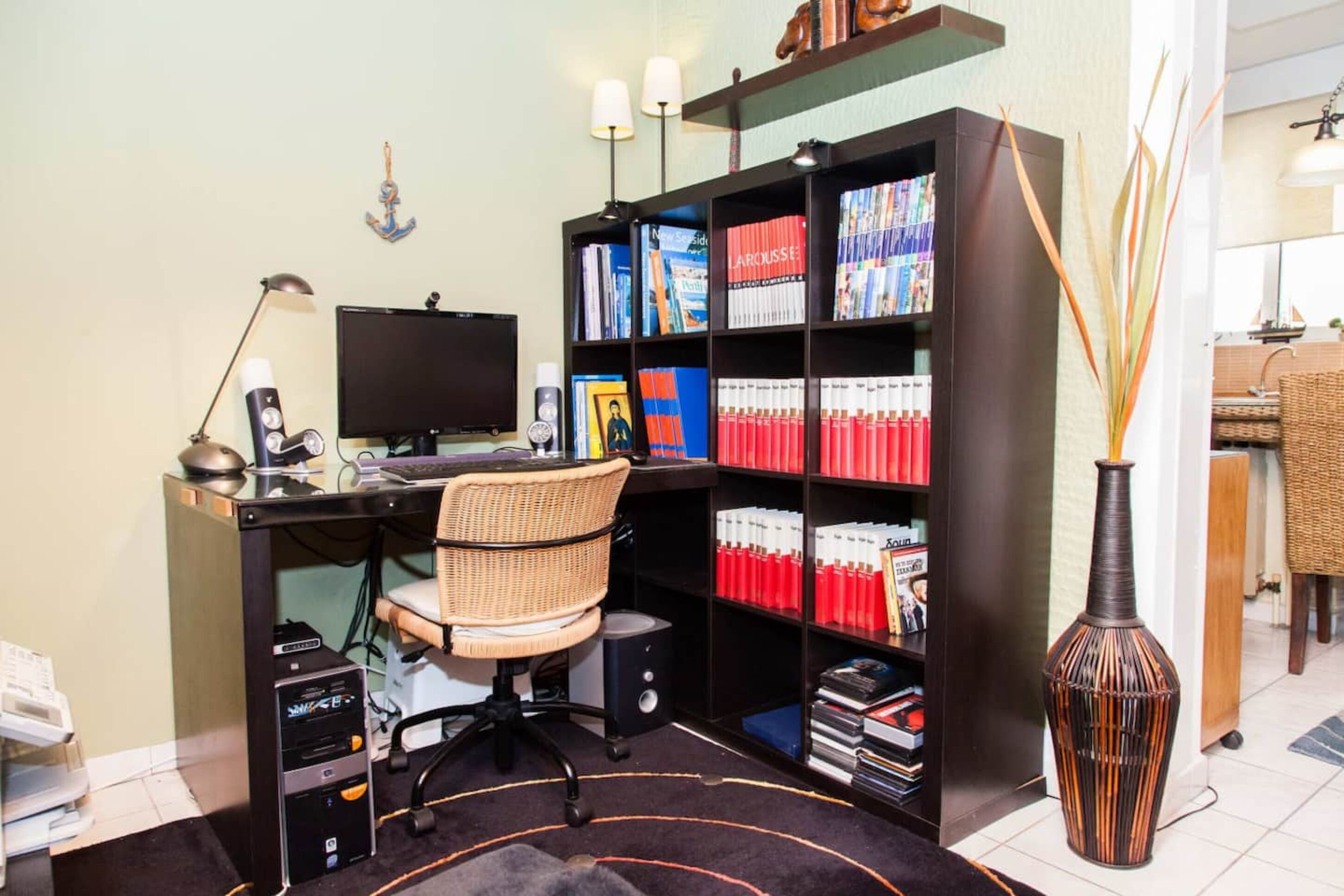 A home office with a desk, computer, chair, bookshelf, and decorative vase.