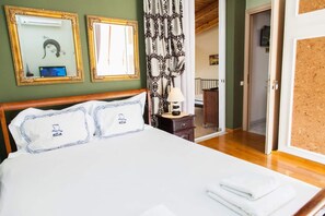 A neatly made bed with white linens and blue embroidered pillows, a bedside table with a lamp, and a mirror on the wall. - Amazing apartment with view (Piraeus)