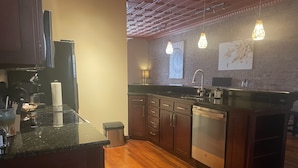 A modern kitchen with wooden cabinets, a black countertop, and a stainless steel dishwasher. - Contemporary apartment on the square! (Neosho)