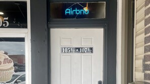 A white door with a neon 'Airbnb' sign above it, and a mailbox on the right. - Contemporary apartment on the square! (Neosho)