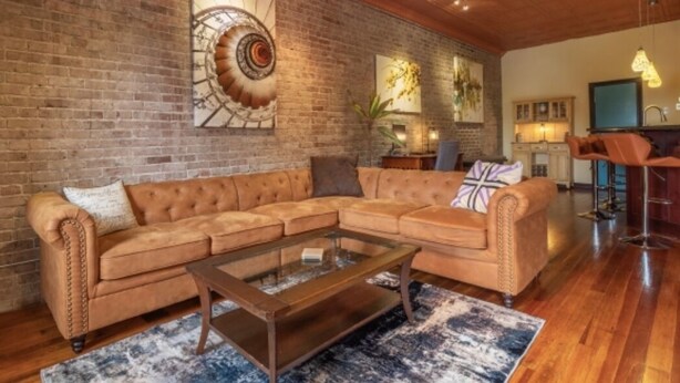 A living room with a brick wall, a sectional sofa, a glass coffee table, and a wooden floor. - Contemporary apartment on the square! (Neosho)