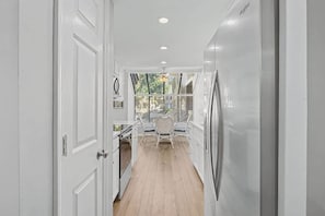 A narrow hallway with white doors, a dining area with a table and chairs, and a view through a window.