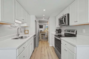 A narrow kitchen with white cabinets, a stainless steel sink, a microwave, and an oven.
