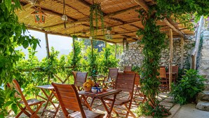 An outdoor seating area with wooden chairs and tables, surrounded by greenery and a stone wall. - Independent house with access to a panoramic lemon grove on the Amalfi Coast! (Scala)
