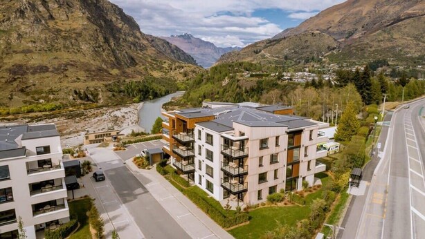 A modern apartment complex with multiple balconies, a river in the background, and a mountainous landscape. - Penthouse Leisure at La Residence du Parc (Queenstown)