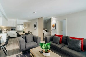 A modern living room with a sofa set, a coffee table with a plant, and a kitchen area in the background.