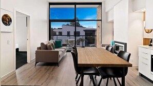 A modern living room with a large window, a sofa, a dining table, and a kitchen area. - Penthouse Leisure at La Residence du Parc (Queenstown)