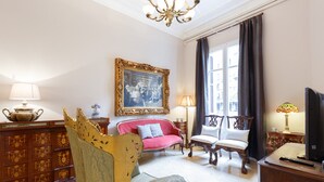 Een kamer met een bank, stoelen, een tafel, een lamp en een schilderij aan de muur.