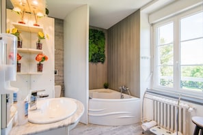 A modern bathroom with a bathtub, a large window, and a wall-mounted plant.