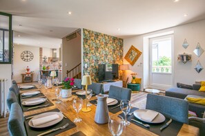 A dining area with a long table set for six, a television, and a patterned wall.