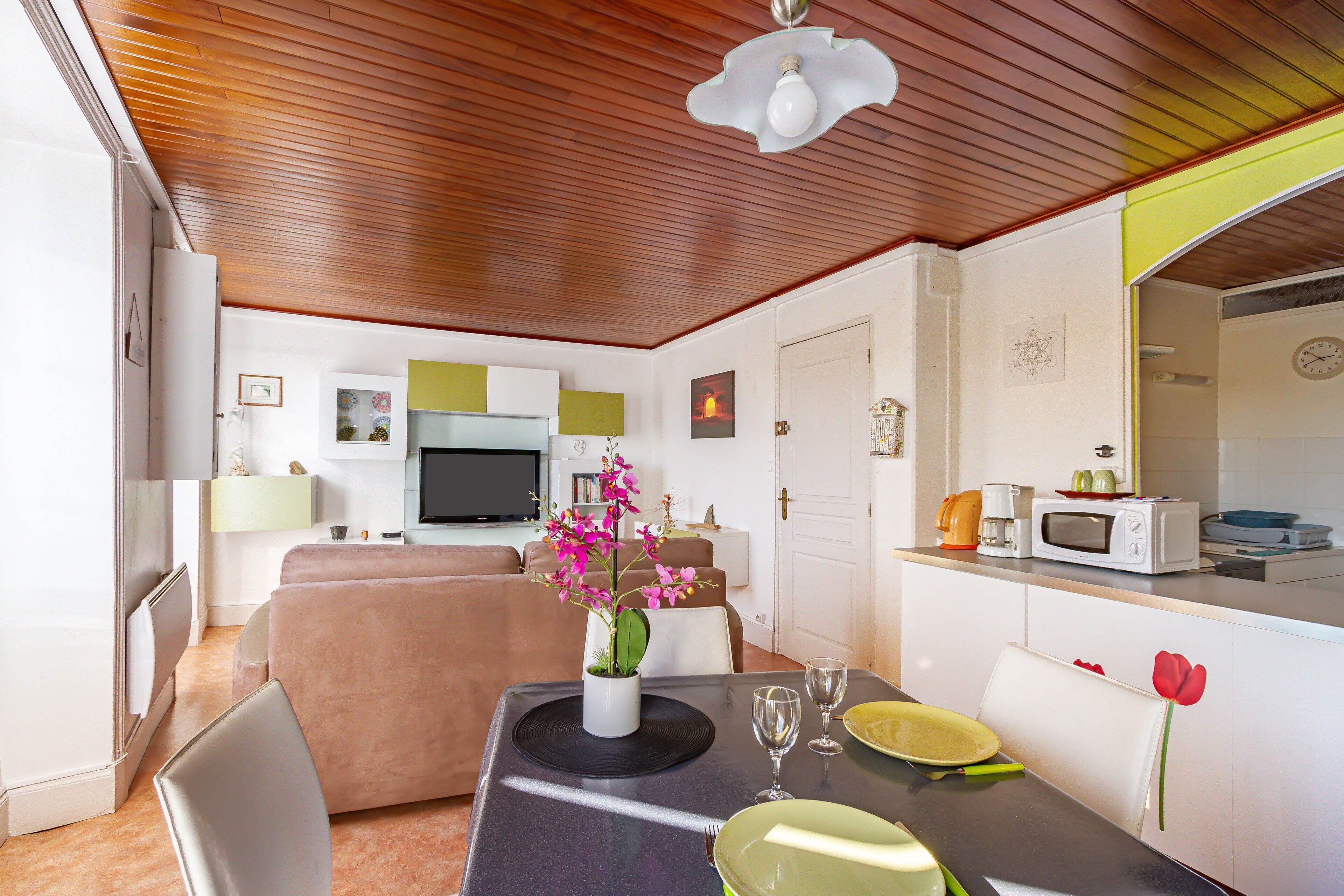 A modern kitchen with a microwave, toaster, and coffee maker. There is a dining table with a vase of flowers and a plate.