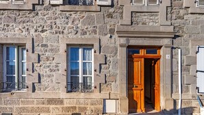 A stone building with a wooden door, windows with shutters, and a small balcony with metal railings. - Le Barry - Studio avec jardin (Murat)