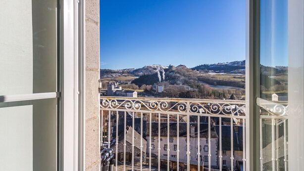 A balcony with a view of a mountainous landscape and a building with smoke rising. - Le Barry - Studio avec jardin (Murat)