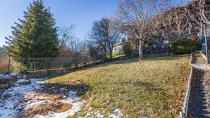 A residential area with a grassy lawn, a stone wall, and a large evergreen tree. - Le Barry - Studio avec jardin (Murat)