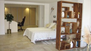 Une chambre à coucher avec un lit, une bibliothèque en bois, une plante en pot et une chaise.