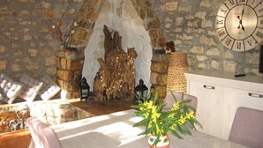 Un mur de pierres rustiques surmonté d’une arche en bois, une grande horloge murale et une table ornée d’un vase de fleurs.