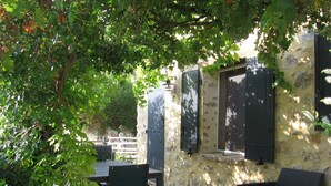 Une terrasse extérieure avec une table et des chaises, un mur en pierre et une fenêtre avec des volets.