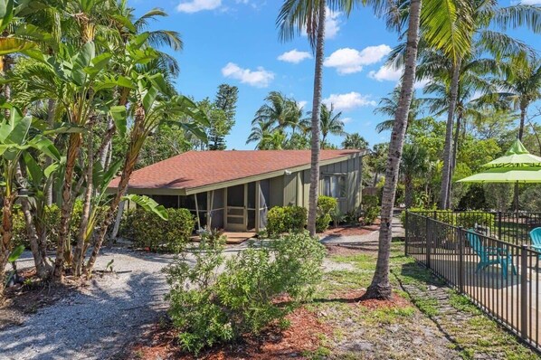 A house with a red roof, surrounded by palm trees and a fenced patio area.