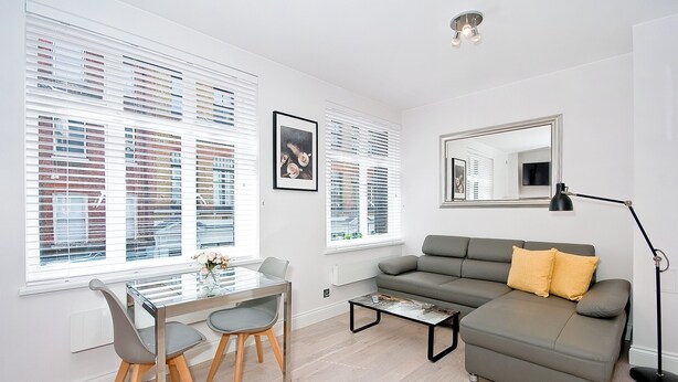 Een moderne woonkamer met een grijze bank, een glazen eettafel met stoelen, en een vloerlamp.