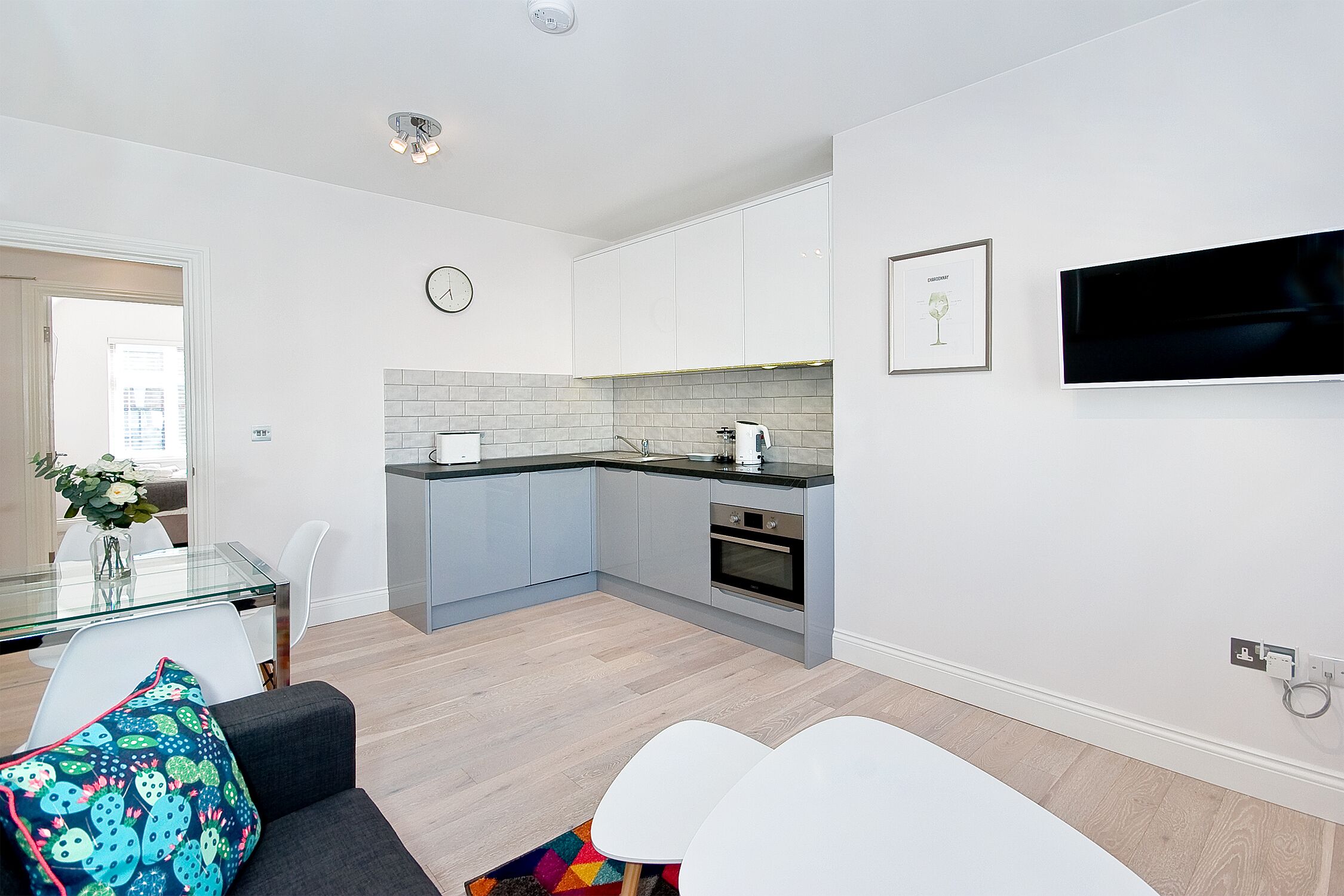 A modern kitchen with white cabinets, a built-in oven, and a flat-screen TV mounted on the wall.