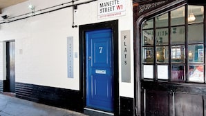 Een gebouw met een blauwe deur waarop '7' staat en een bord erboven met de tekst 'Manette Street W1, City of Westminster'.