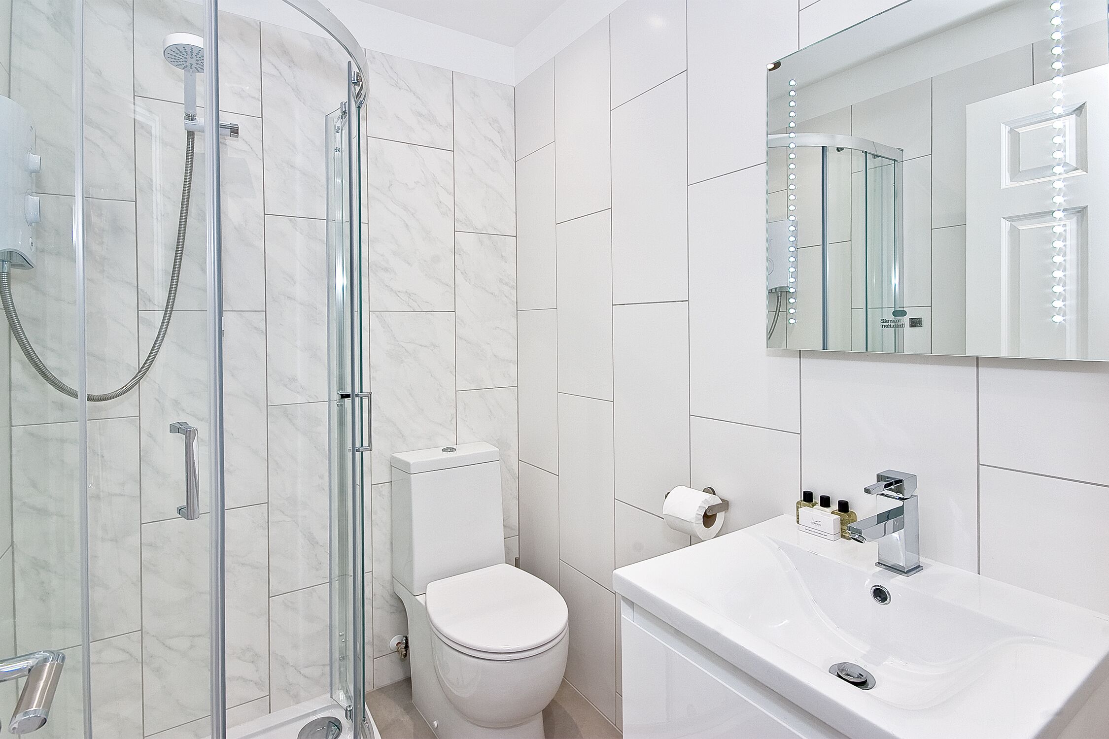 A modern bathroom with a glass-enclosed shower, a white toilet, and a sink with a mirror above it.