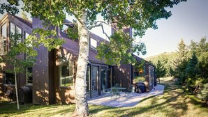 A modern house with large windows, a patio with outdoor furniture, and a tree in the foreground. - The Silver Spur | 5BR Cabin, Walk to PCMR (Park City)