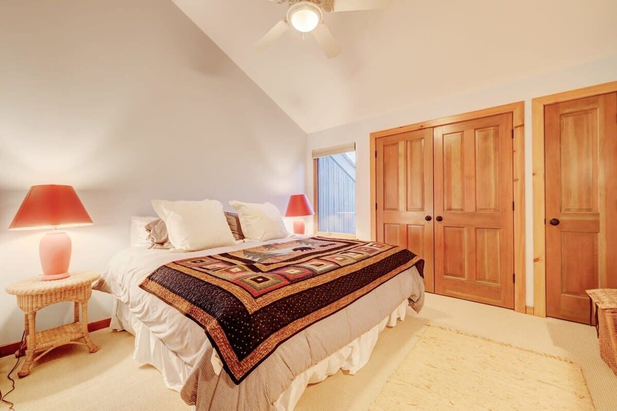 A bedroom with a large bed, two bedside lamps, a ceiling fan, and wooden doors.