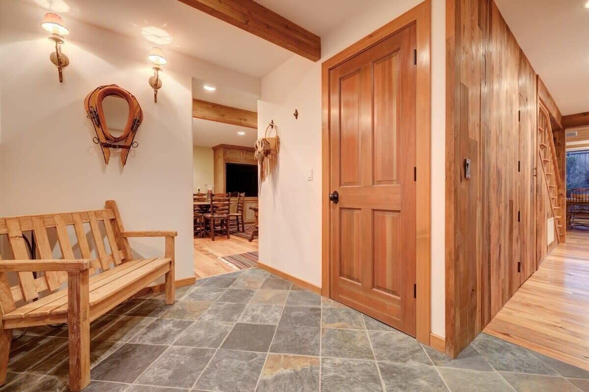 A wooden bench, a large wooden door, and a stone-tiled floor in a hallway.