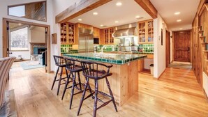 A modern kitchen with wooden cabinets, a green island with bar stools, and a large window. - The Silver Spur | 5BR Cabin, Walk to PCMR (Park City)