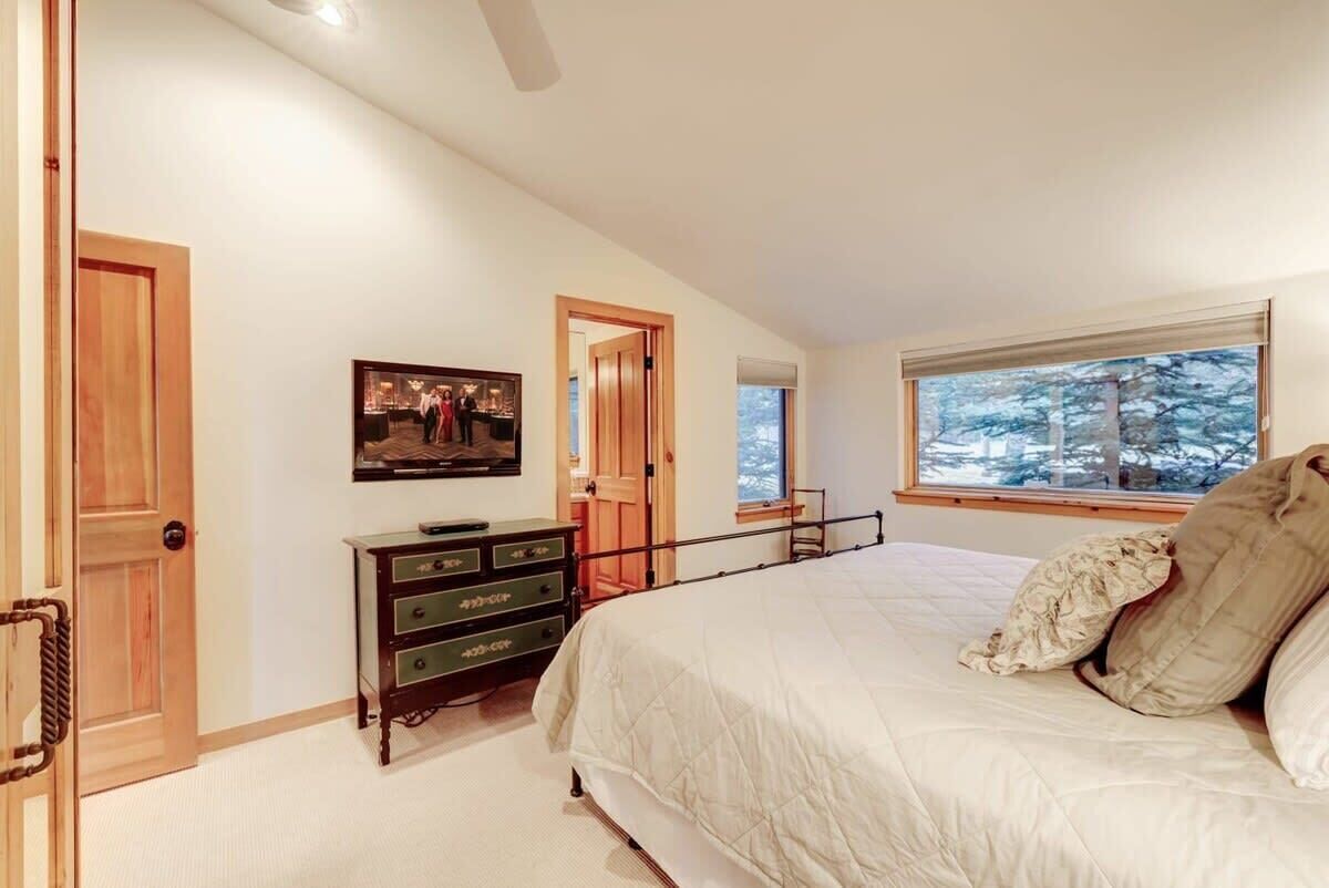 A bedroom with a large bed, a dresser, a painting on the wall, and a window with a view of trees.