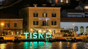 A hotel named "HOTEL TISNO" with a prominent illuminated sign, a waterfront view, and boats docked in the background. - Villa Pina Tisno TOP**** Apartment Luca 4-6 Persons (Tisno)