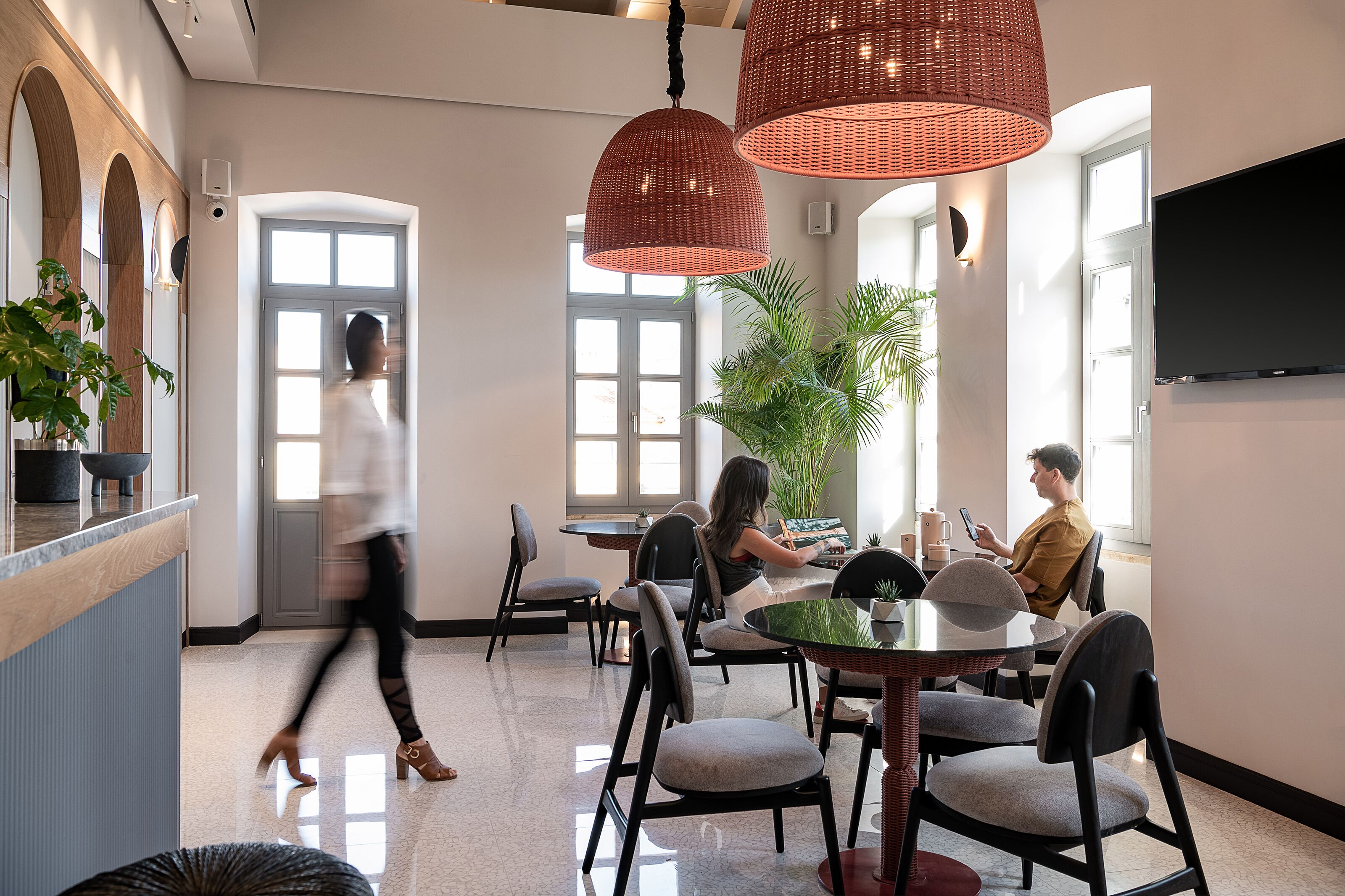 A modern dining area with round tables, black chairs, and red wicker pendant lights.