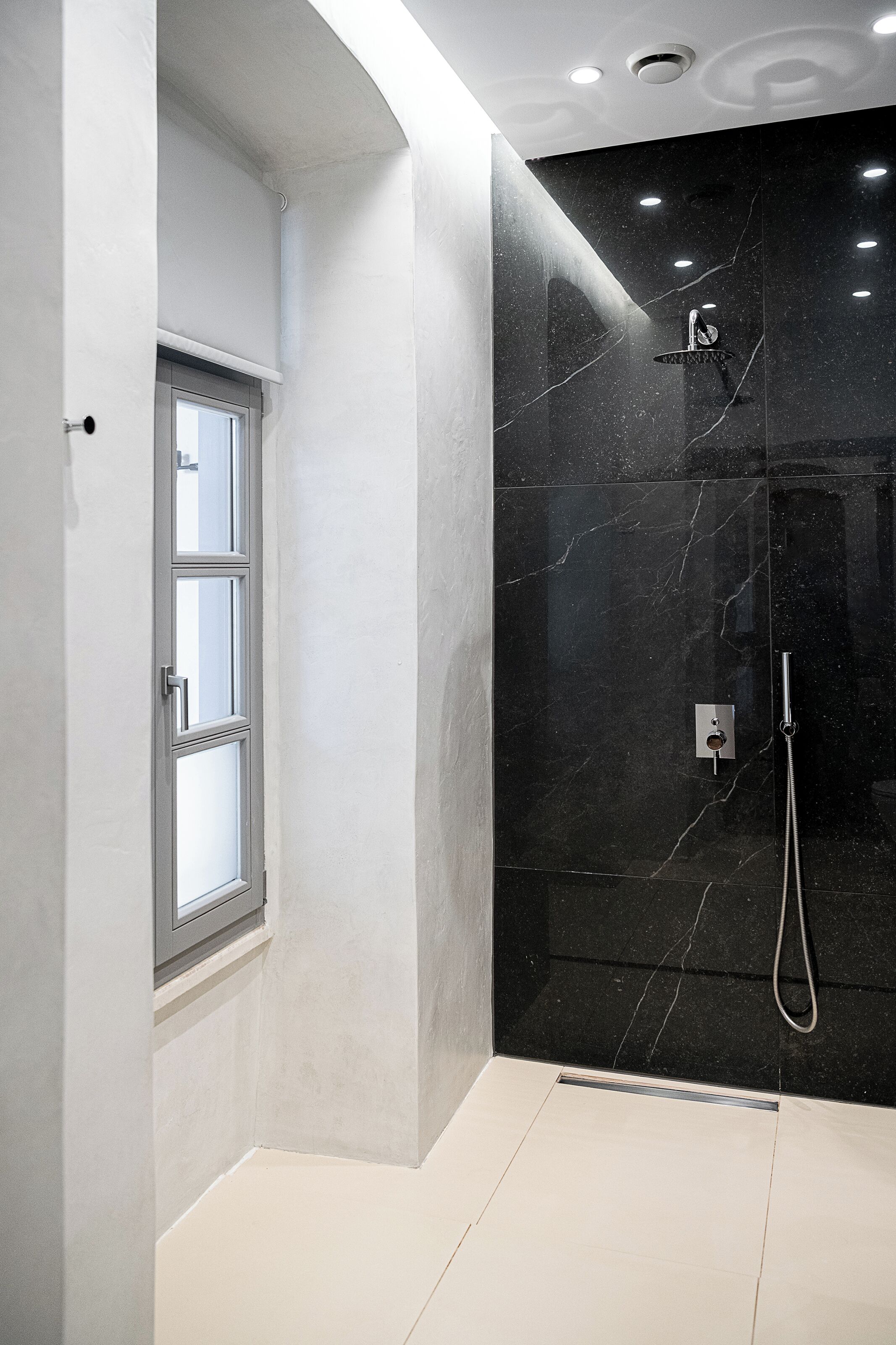Un baño moderno con ducha, ventana y pared de mármol.