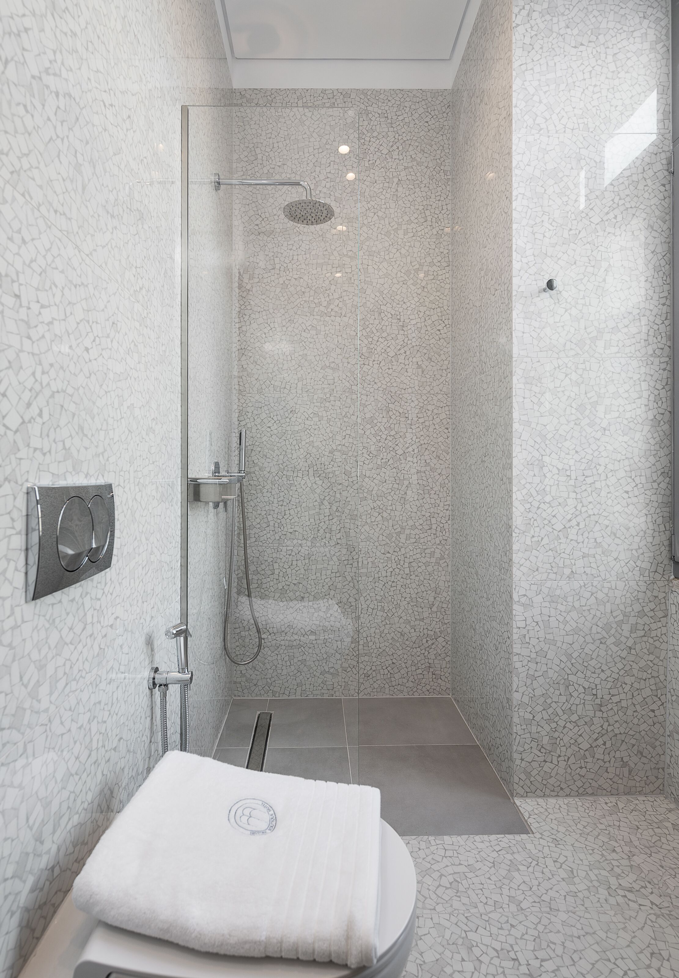 Un baño moderno con ducha envuelta en vidrio, un lavamanos blanco y una toalla sobre la encimera.