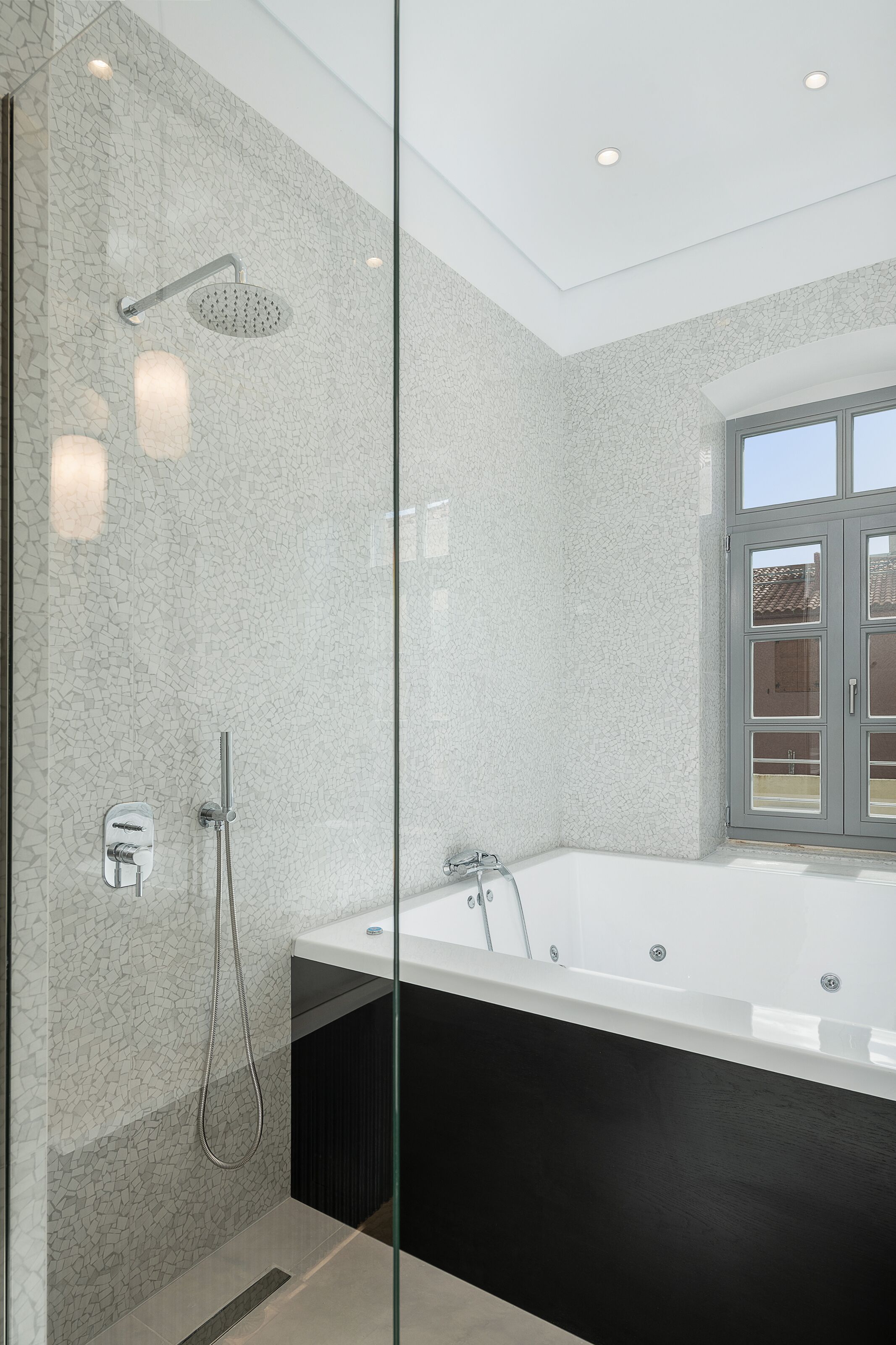 Un baño moderno con ducha envuelta en vidrio, una bañera amplia y una ventana con vistas al exterior.