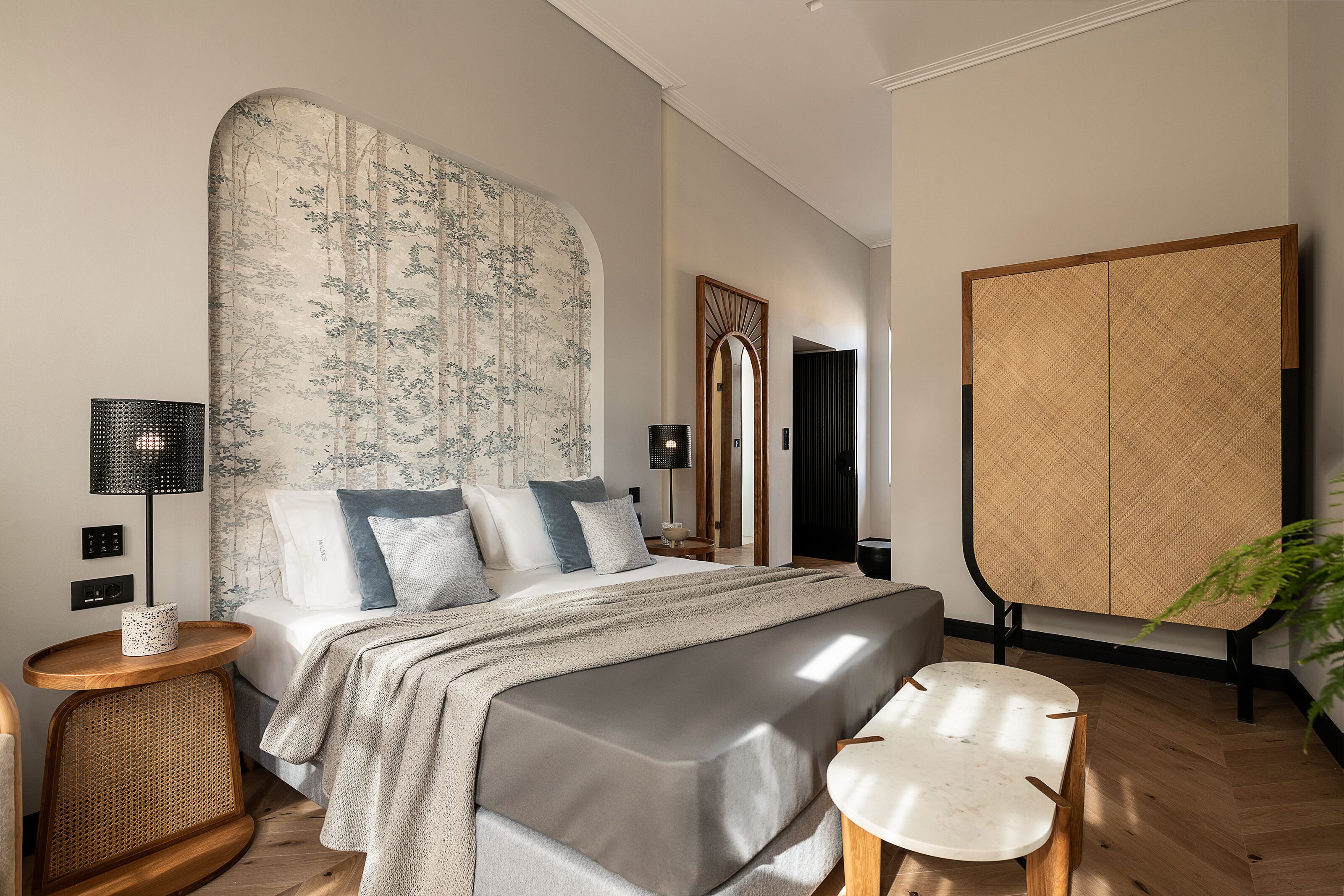 A modern bedroom with a large bed, bedside tables, a mirror, and a wardrobe.