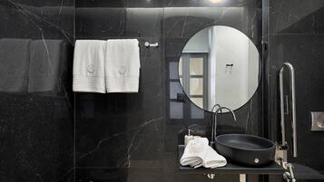 A modern bathroom with a black marble wall, a round mirror, a black sink, and two white towels.