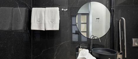 A modern bathroom with a black marble wall, a round mirror, a black sink, and two white towels.